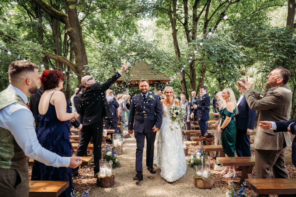 Bride and groom walking down outdoor aisle.
