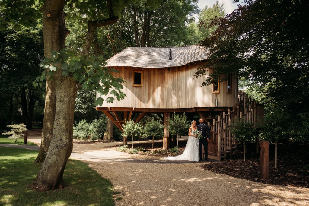 Couple standing by elevated wooden treehouse in forest.