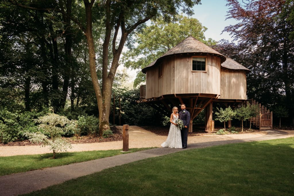 Couple posing in front of a wooden treehouse.