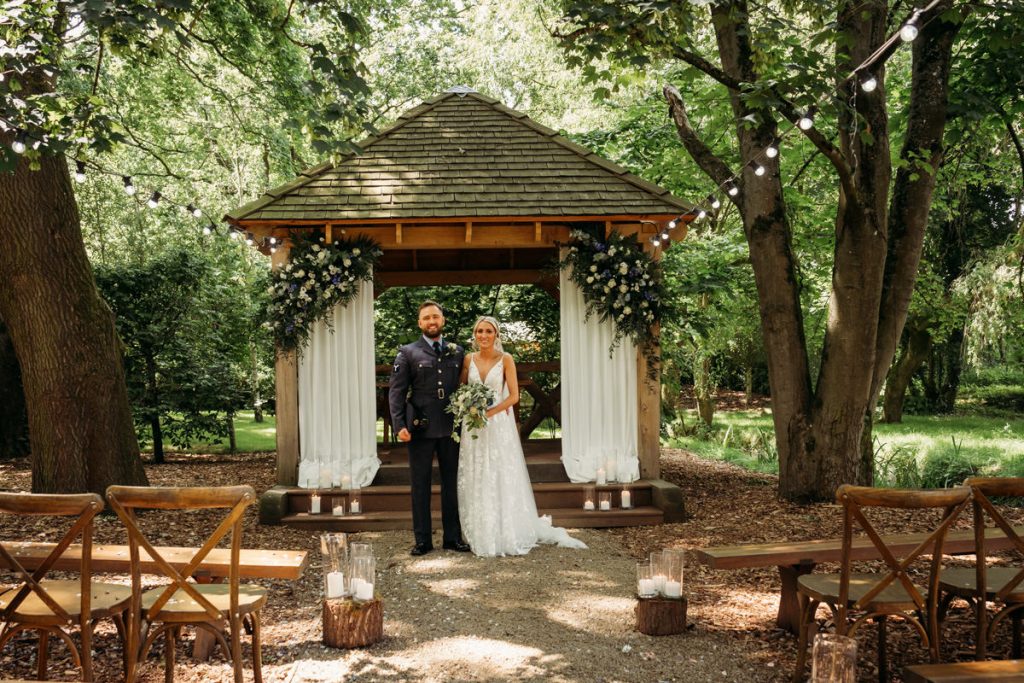 Outdoor wedding ceremony at woodland venue with couple.