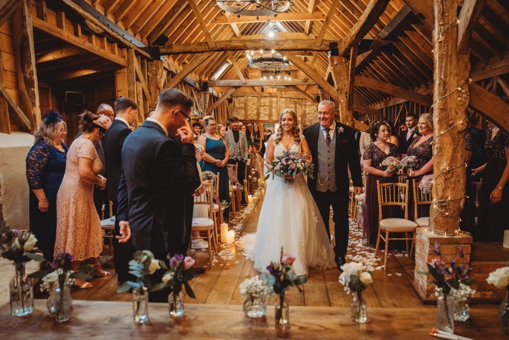 Bride walking down barn wedding aisle with guests.