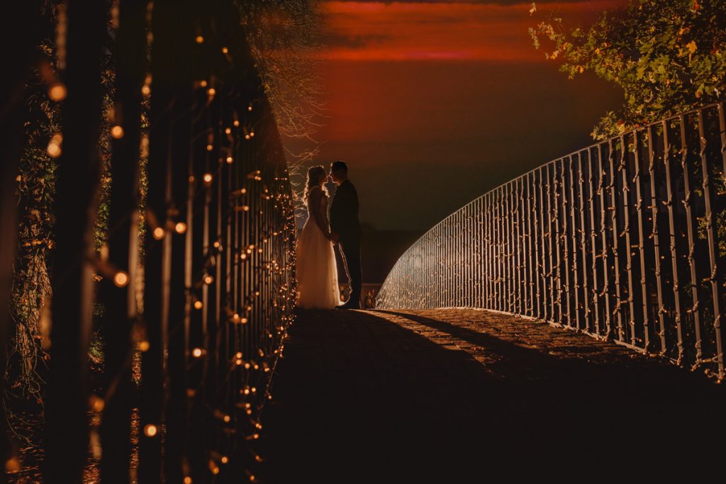 Couple silhouetted on illuminated bridge at sunset.