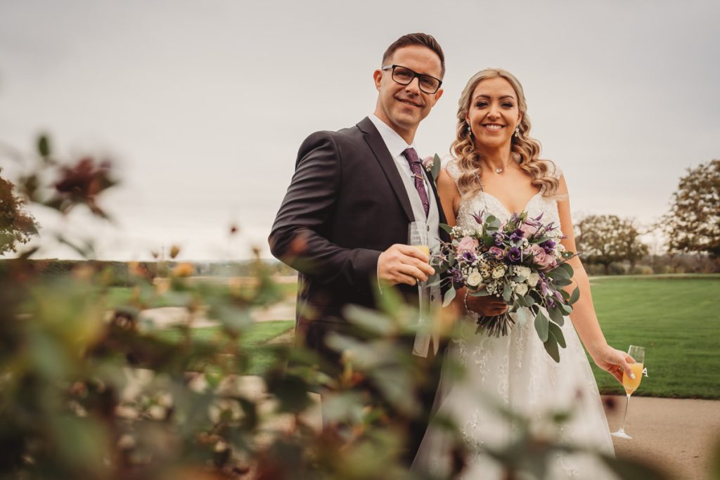 Smiling couple at outdoor wedding with bouquet.