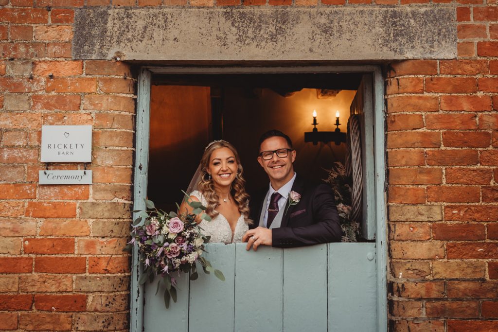 Smiling couple at rustic wedding venue window.