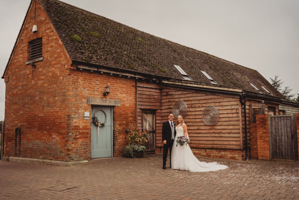 Bride and groom by rustic brick building.