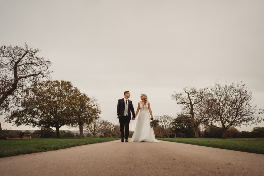 Newlyweds walking on road, autumn trees surrounding them.