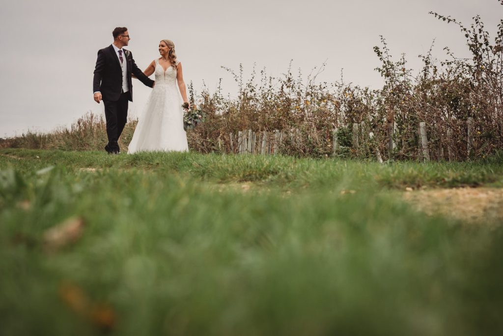 Bride and groom walking on grassy path.