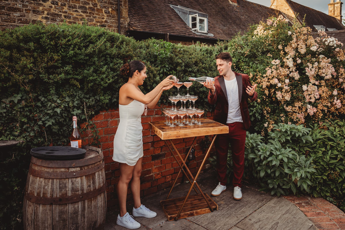 Couple pouring champagne into glass tower outdoors.
