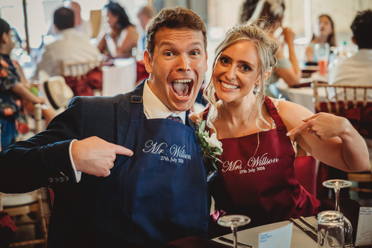 Smiling couple wearing personalised aprons at wedding reception.