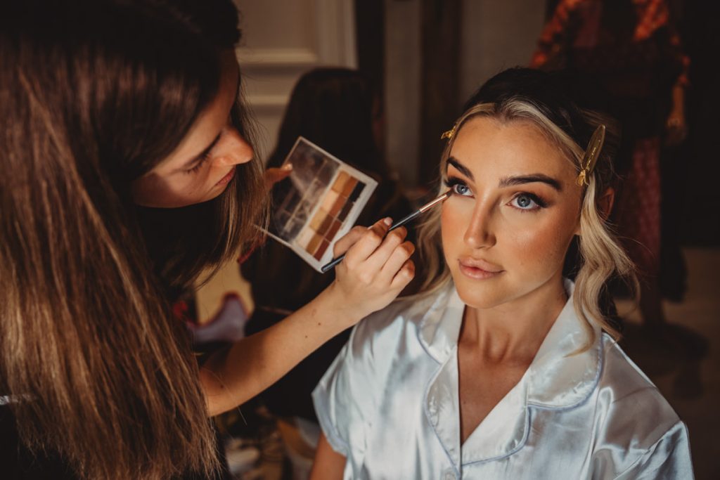 Makeup artist applying eyeshadow to woman in robe.