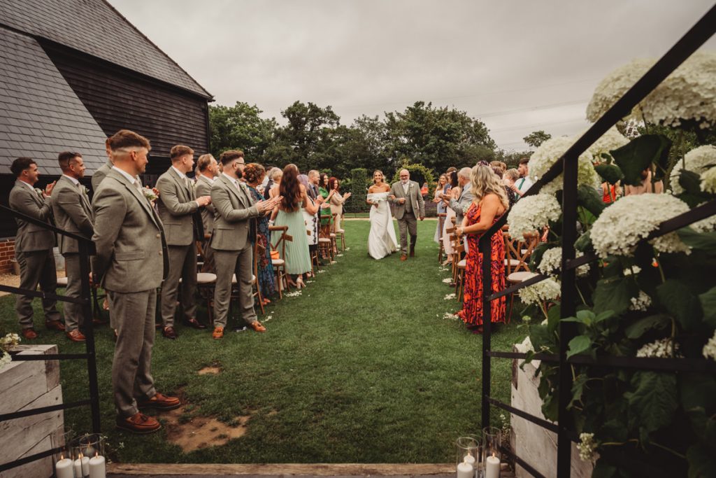 Bride walking down the aisle with father, outdoor wedding.
