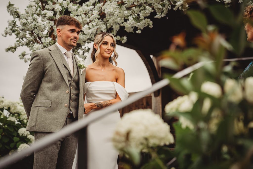 Bride and groom standing under floral archway.
