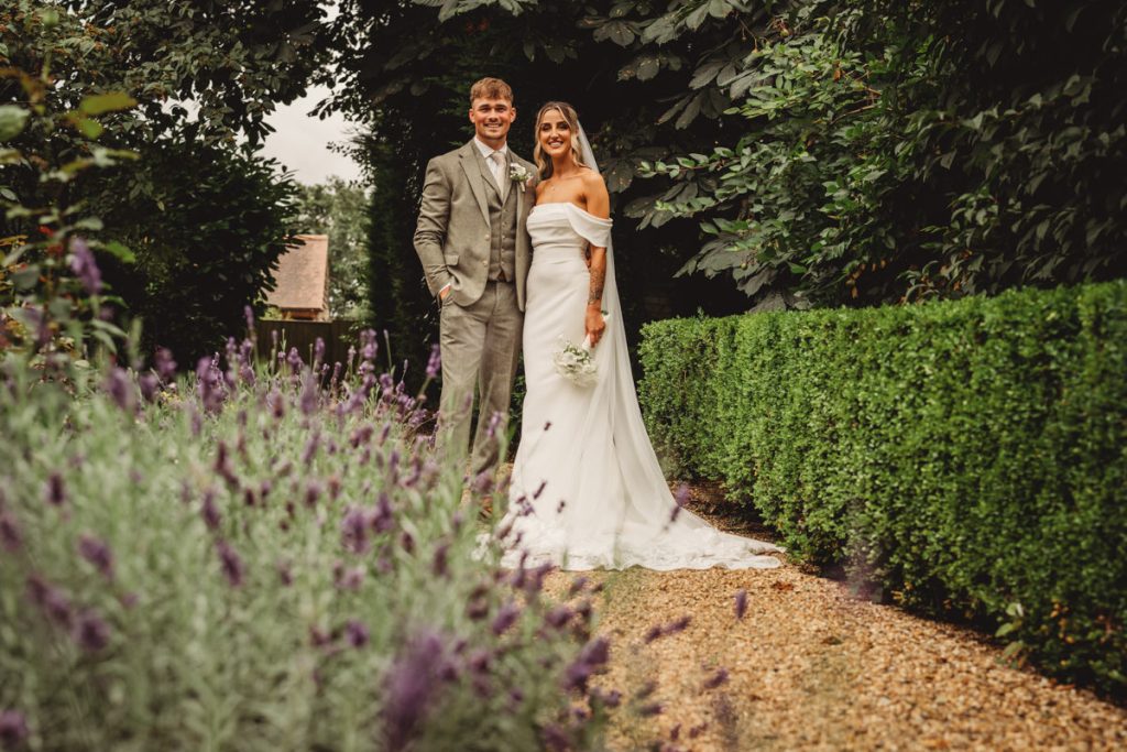 Couple in wedding attire in a garden pathway.
