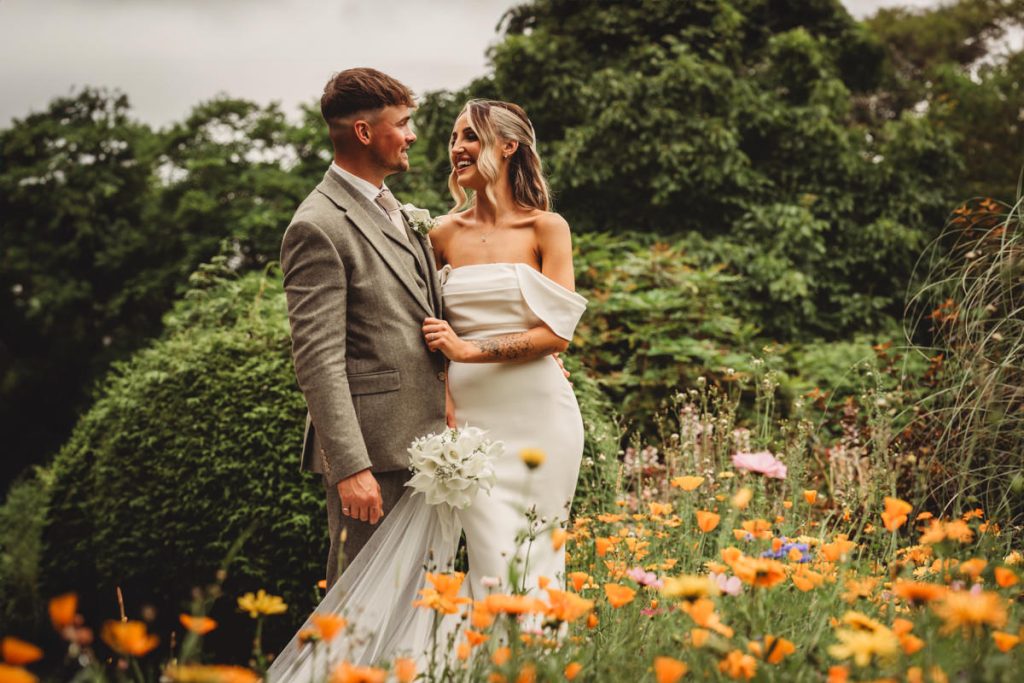 Bride and groom in floral garden, smiling happily.