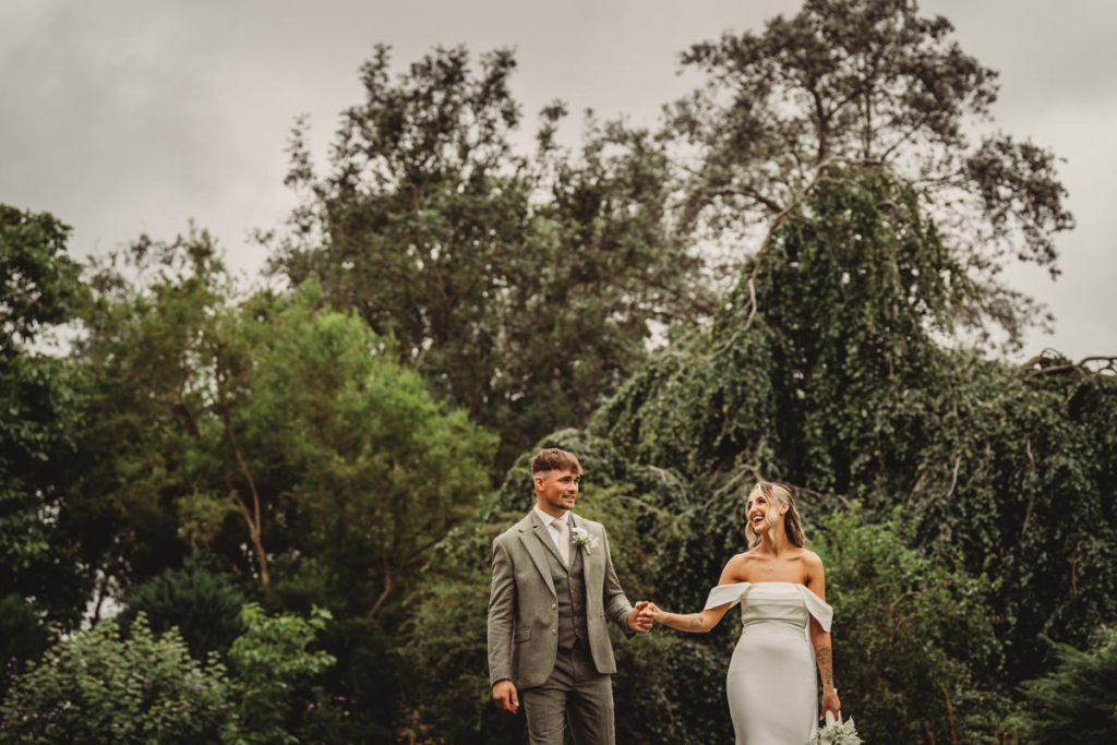 Bride and groom holding hands in lush garden.