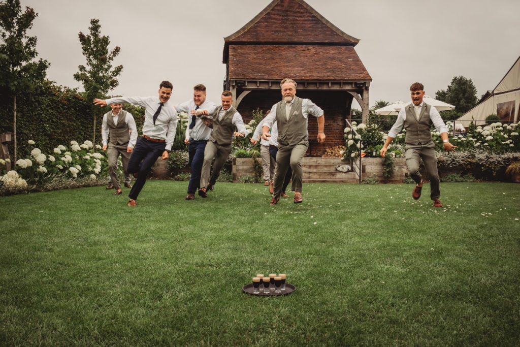 Groomsmen racing towards a tray of drinks on lawn.