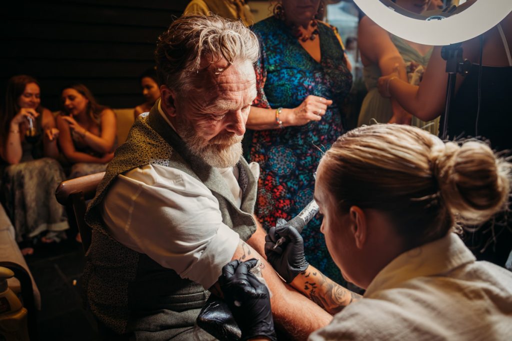 Tattoo artist working on man's arm at event.