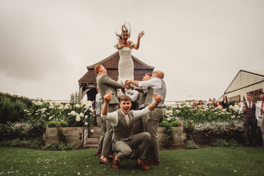 Bride tossed by groomsmen in garden wedding celebration.