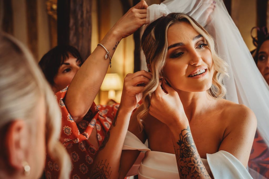 Bride preparing with friends, adjusting veil and earrings.