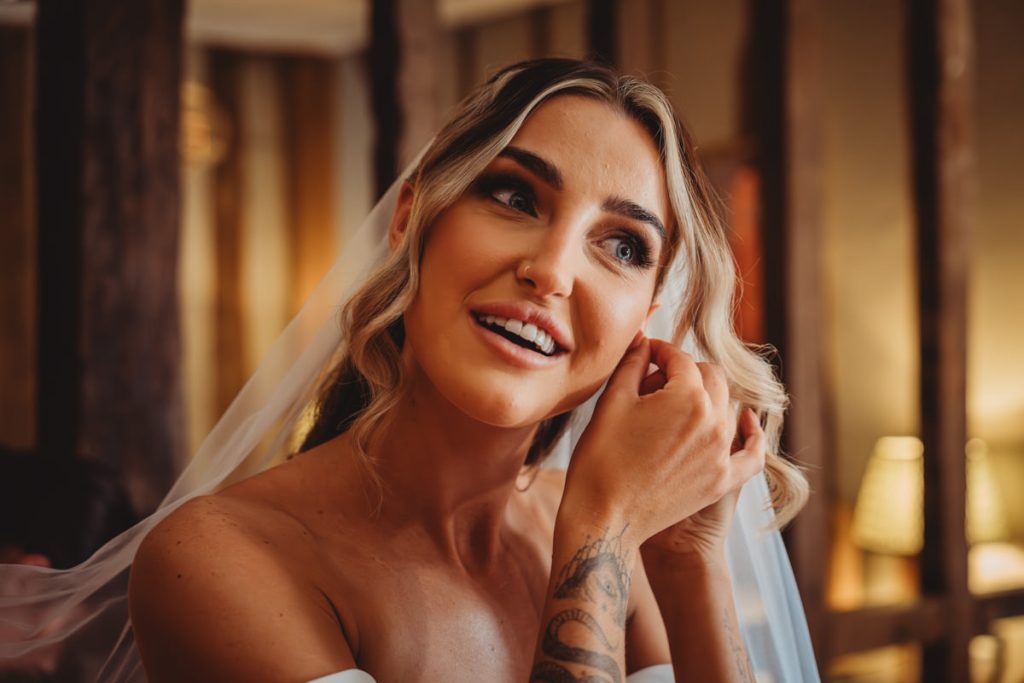 Bride smiling while adjusting earring, tattoo visible