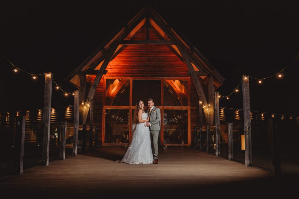 Couple posing outside wooden venue at night.