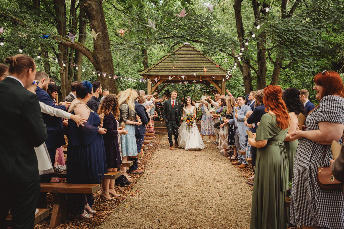 Wedding couple exits outdoor ceremony with confetti celebration.