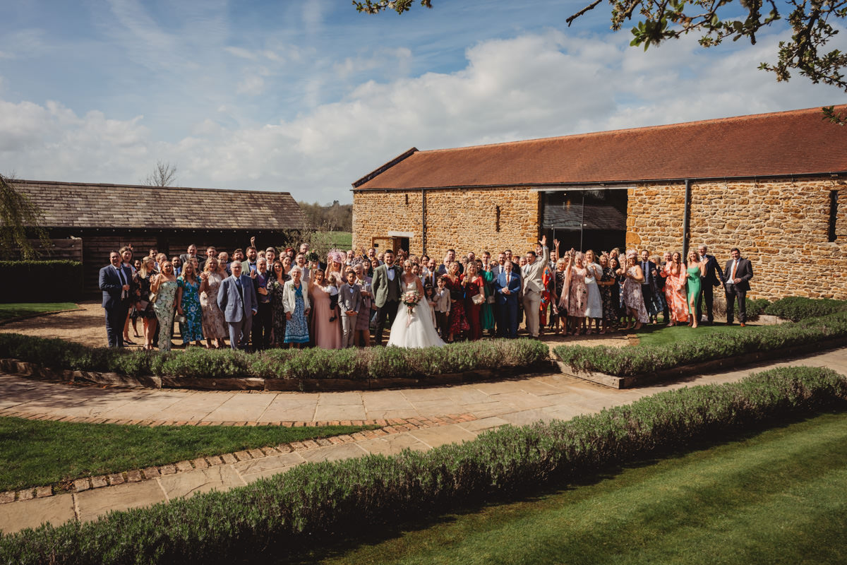 Large wedding group photo outside rustic barn.