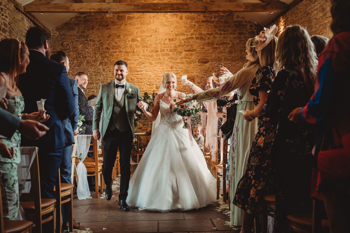 Bride and groom walk through confetti-filled aisle.