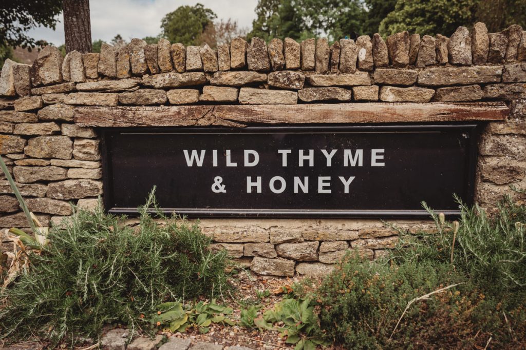 Rustic sign: Wild Thyme & Honey, stone wall background.