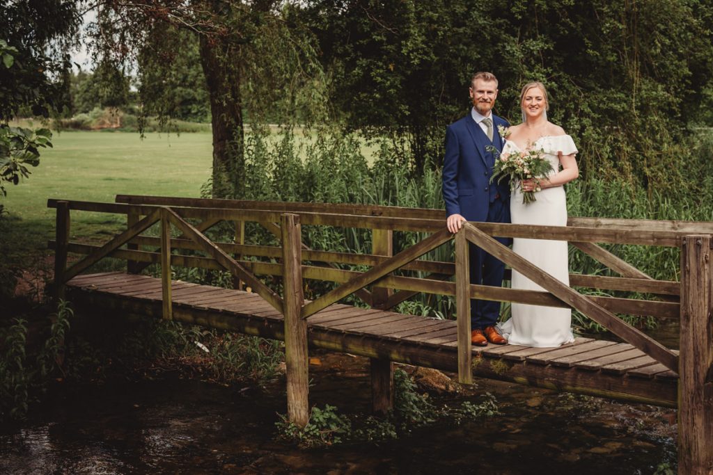 Bride and groom standing on wooden bridge outdoors.