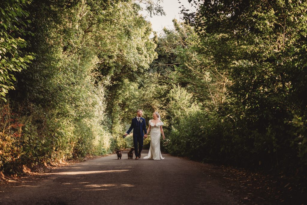 Bride and groom walking with dogs in forest.