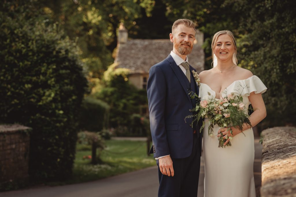 Bride and groom smiling outdoors in wedding attire.