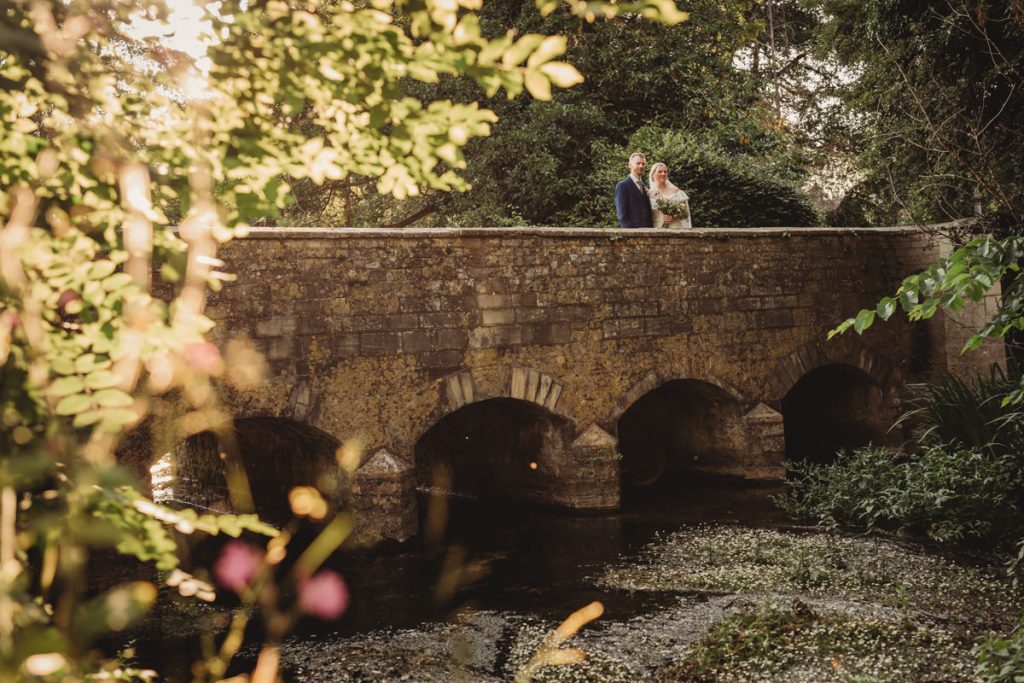 Couple standing on historic stone bridge in sunlight.