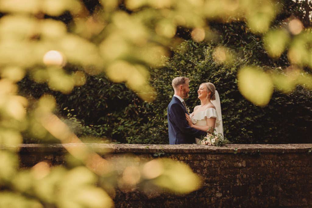 Bride and groom smiling on a stone bridge.