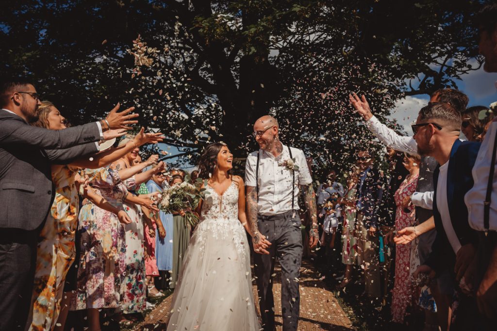 Bride and groom showered with confetti outdoors.
