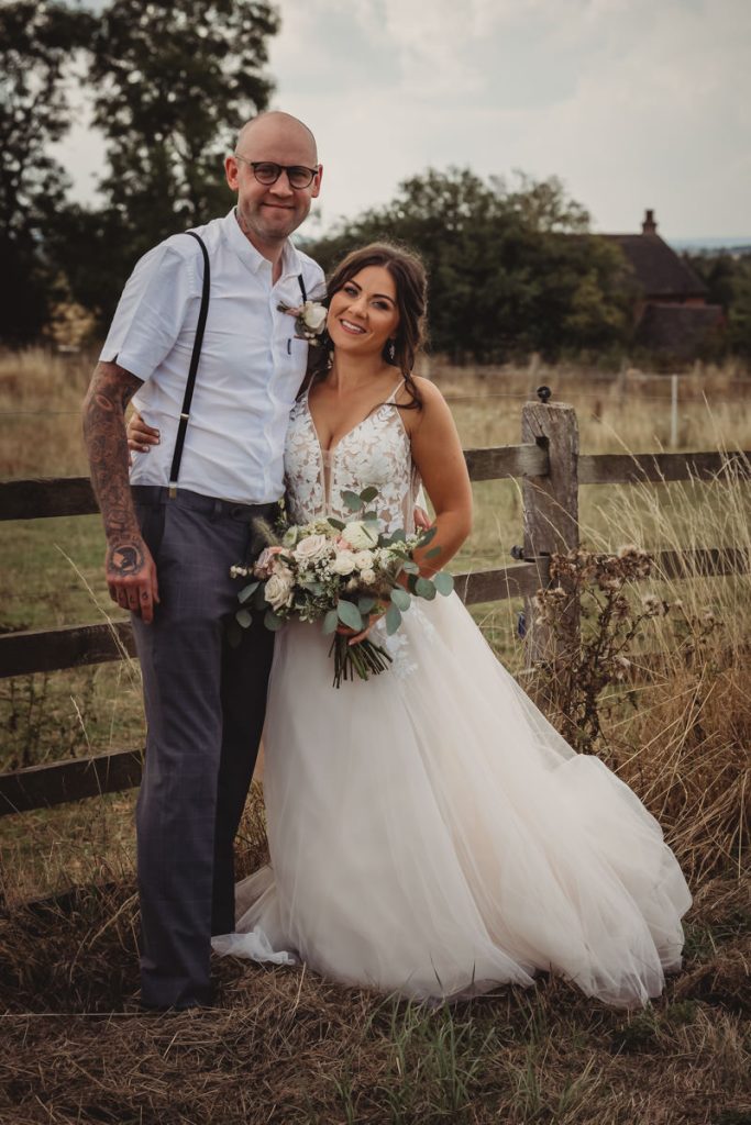 Bride and groom smiling in rustic countryside setting.
