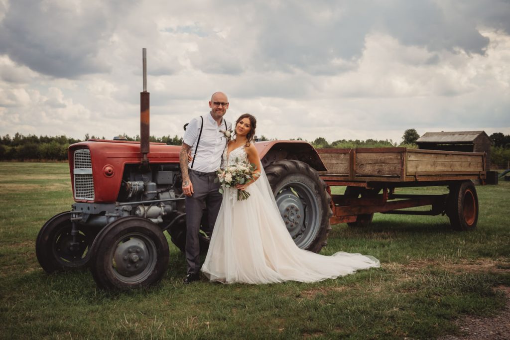 Bride and groom standing by vintage tractor.
