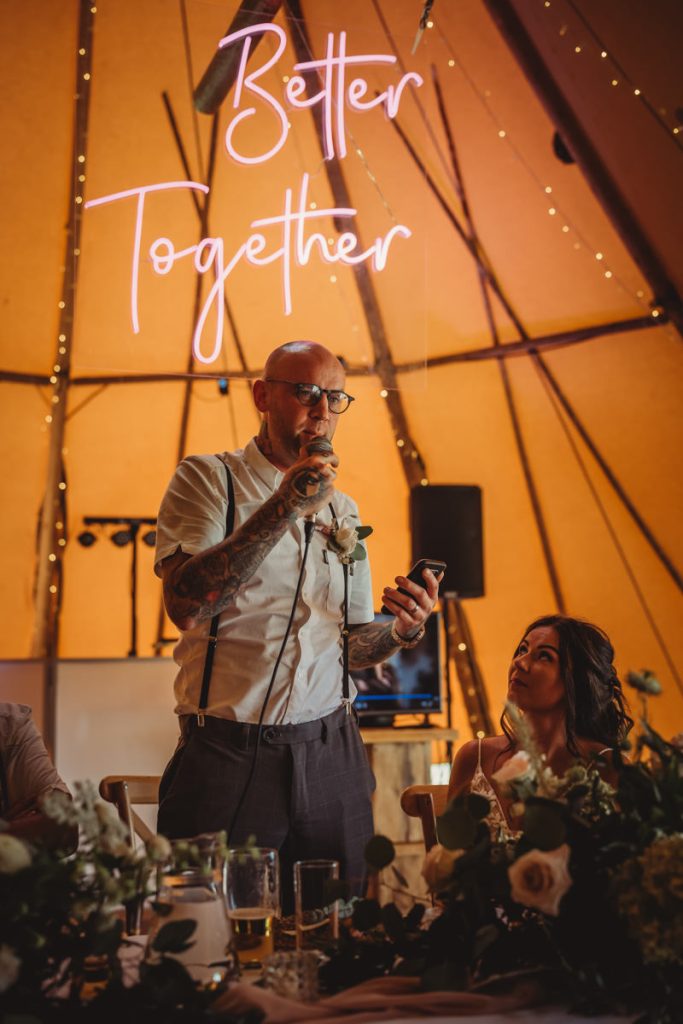 Man giving wedding speech under 'Better Together' sign.