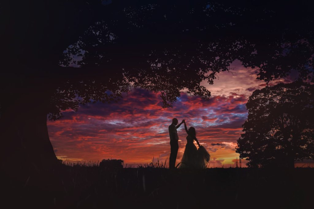 Couple dancing at sunset under silhouetted trees.