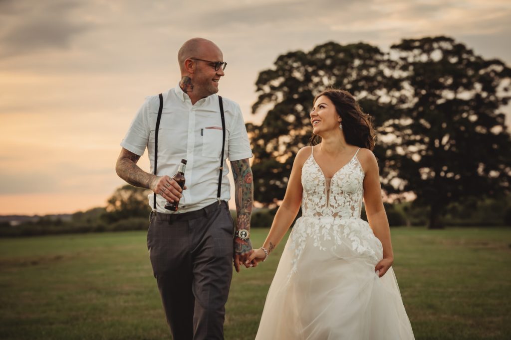 Bride and groom walking in a field at sunset.