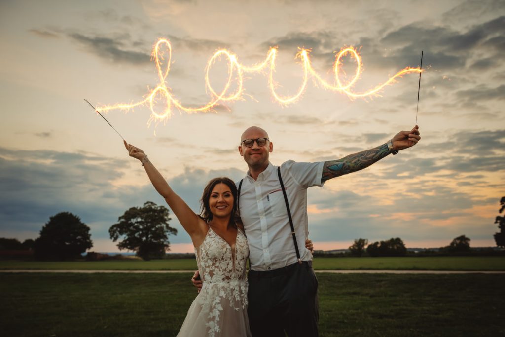 Couple holding sparklers writing 'Love' at sunset.