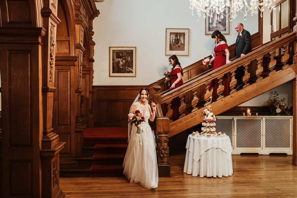 Bride and bridesmaids descending ornate staircase indoors.