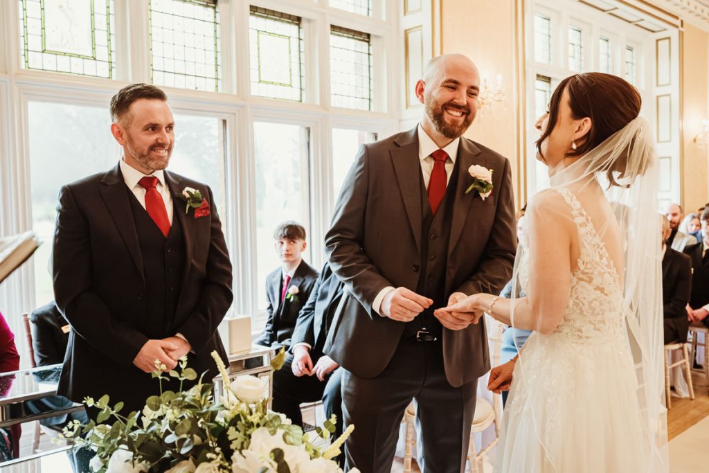 Wedding ceremony, groom smiling at bride exchanging rings.