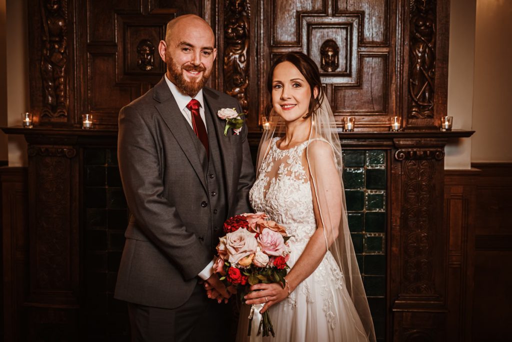 Bride and groom posing with floral bouquet indoors.