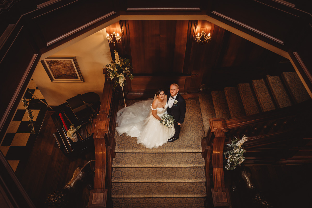 Bride and groom on wooden staircase, elegant interior.