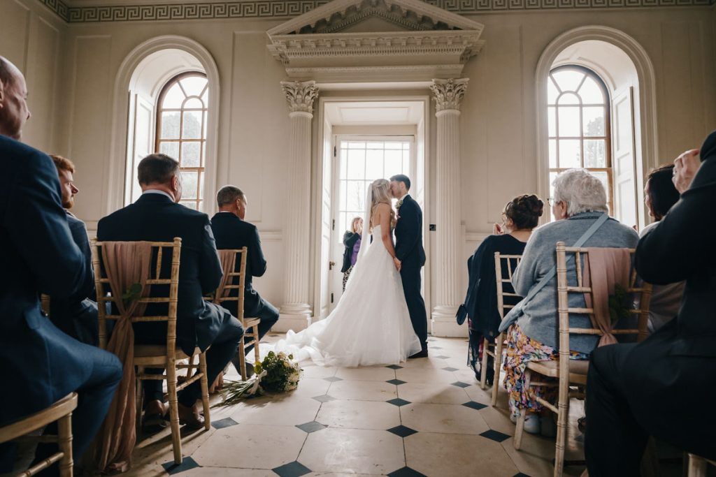 Couple in wedding attire kissing indoors.