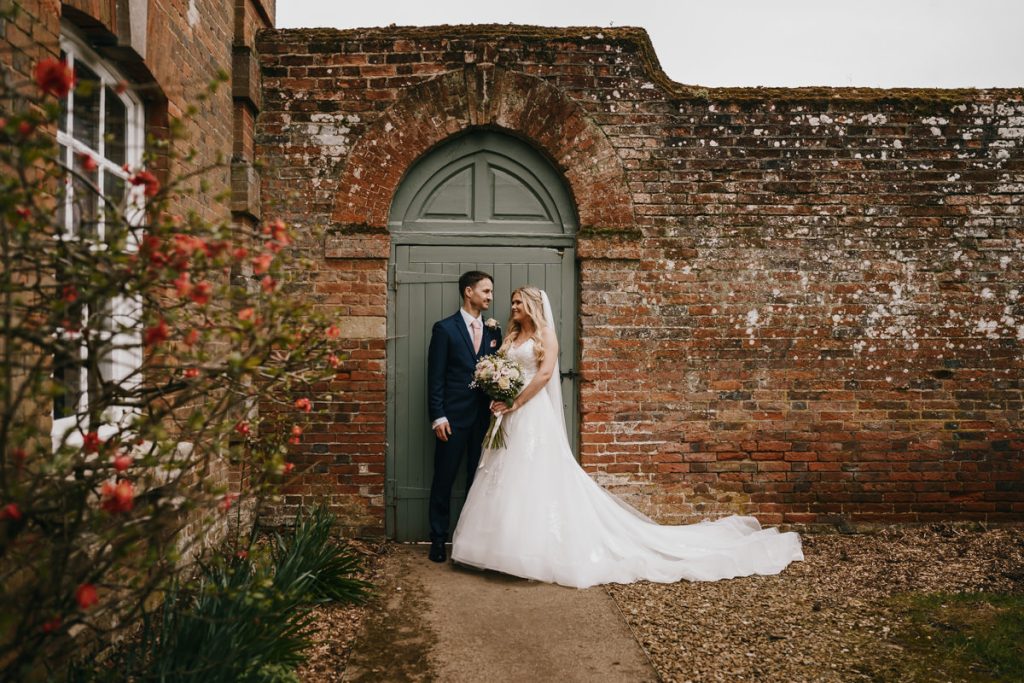 Bride and groom standing by rustic brick wall.