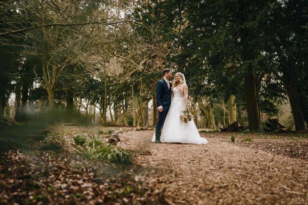 Wedding couple in forest setting, smiling and holding hands.