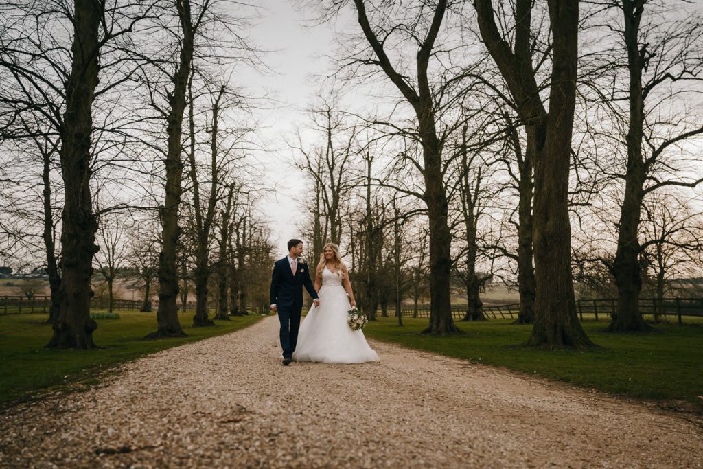 Bride and groom walking along tree-lined path