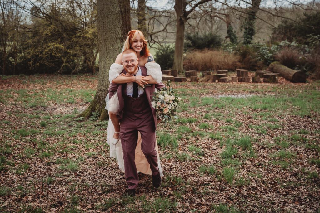 Bride piggybacks groom in forest wedding photoshoot.